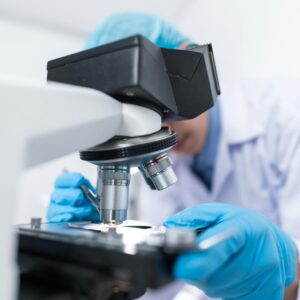 Close-up of a scientist examining samples under a microscope in a lab setting.